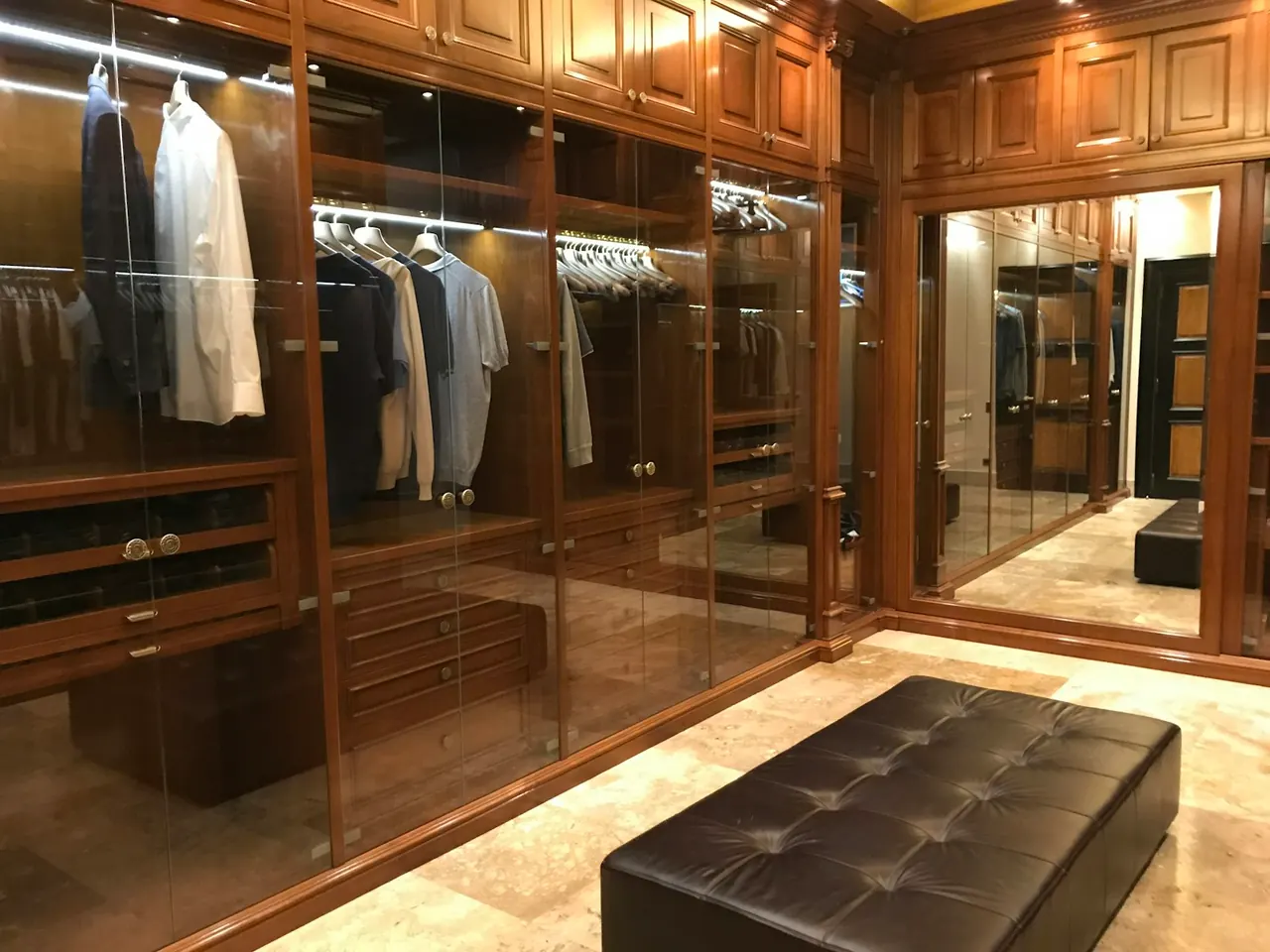 Walk-in closet with glass-front wood wardrobes and a bench