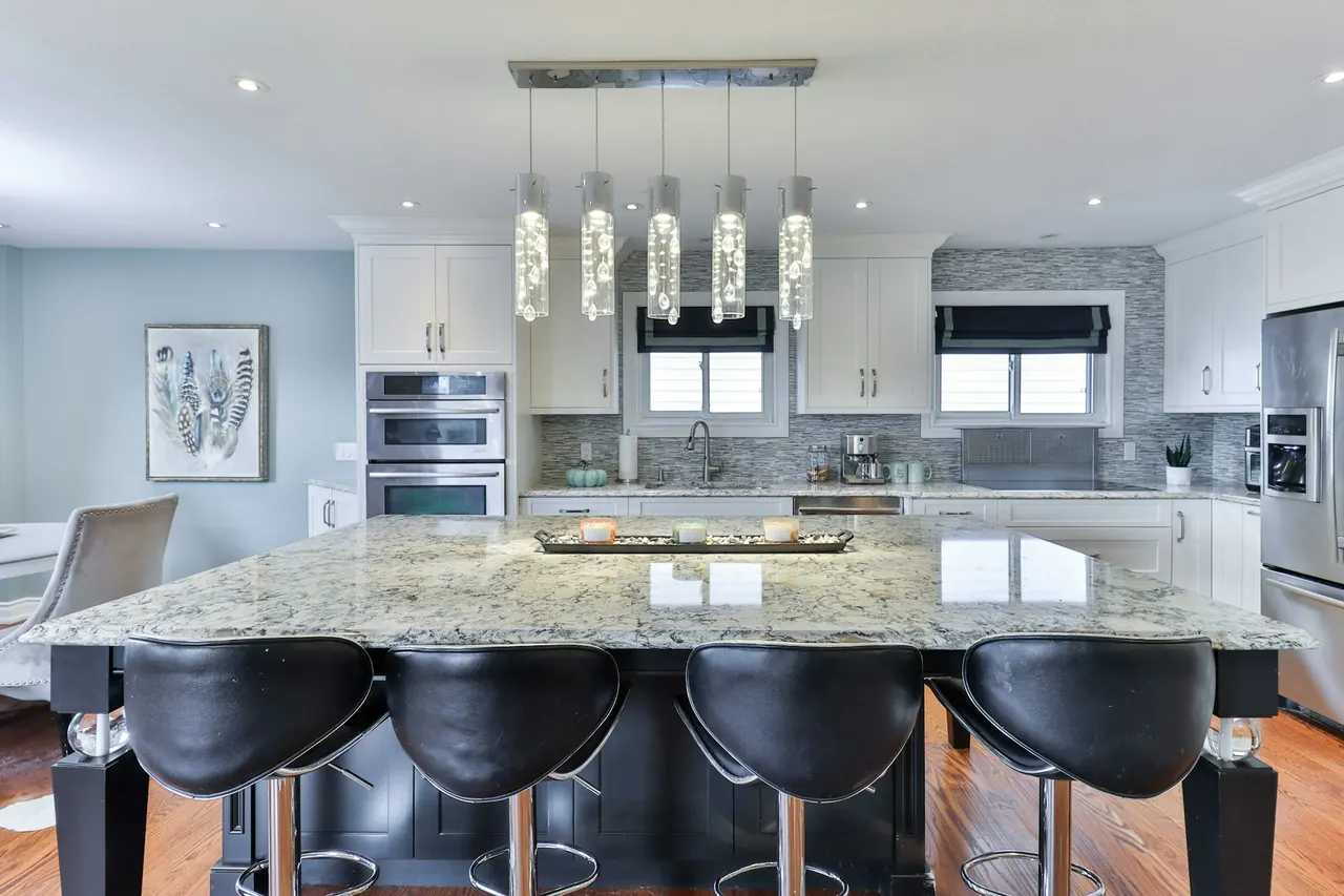 Custom kitchen with white cabinetry, a dark island and pendant lights