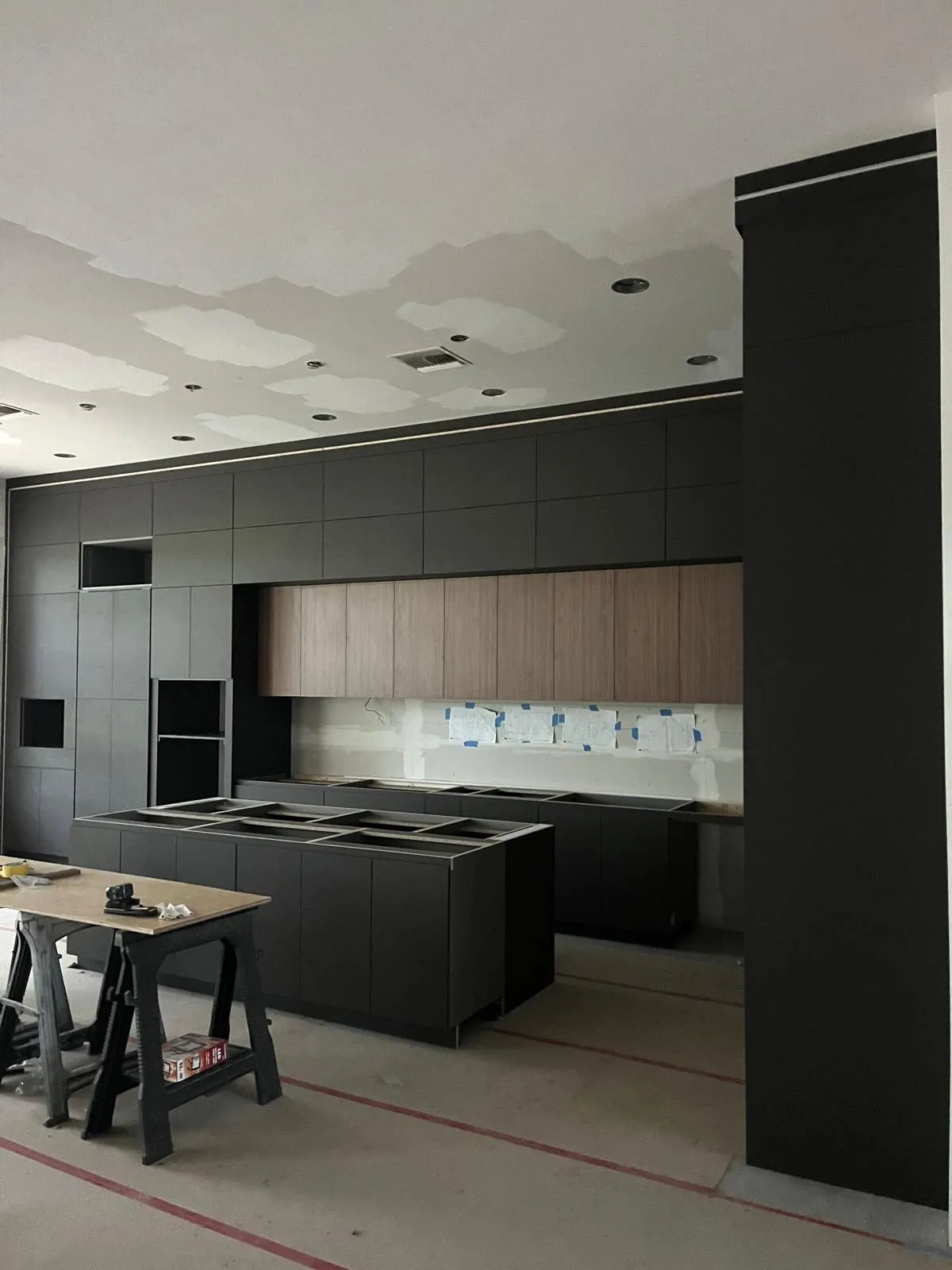 Matte charcoal kitchen with walnut upper cabinets during installation